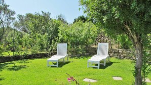 Twee witte lounge stoelen op een verzorgd gazon, met een stenen muur en weelderige begroeiing op de achtergrond.