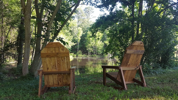 Two wooden Adirondack chairs facing a calm lake surrounded by dense trees. - Backyard splendor!!! (Story)
