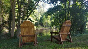Deux fauteuils Adirondack en bois, placés face à un lac paisible, entouré d’une forêt dense.