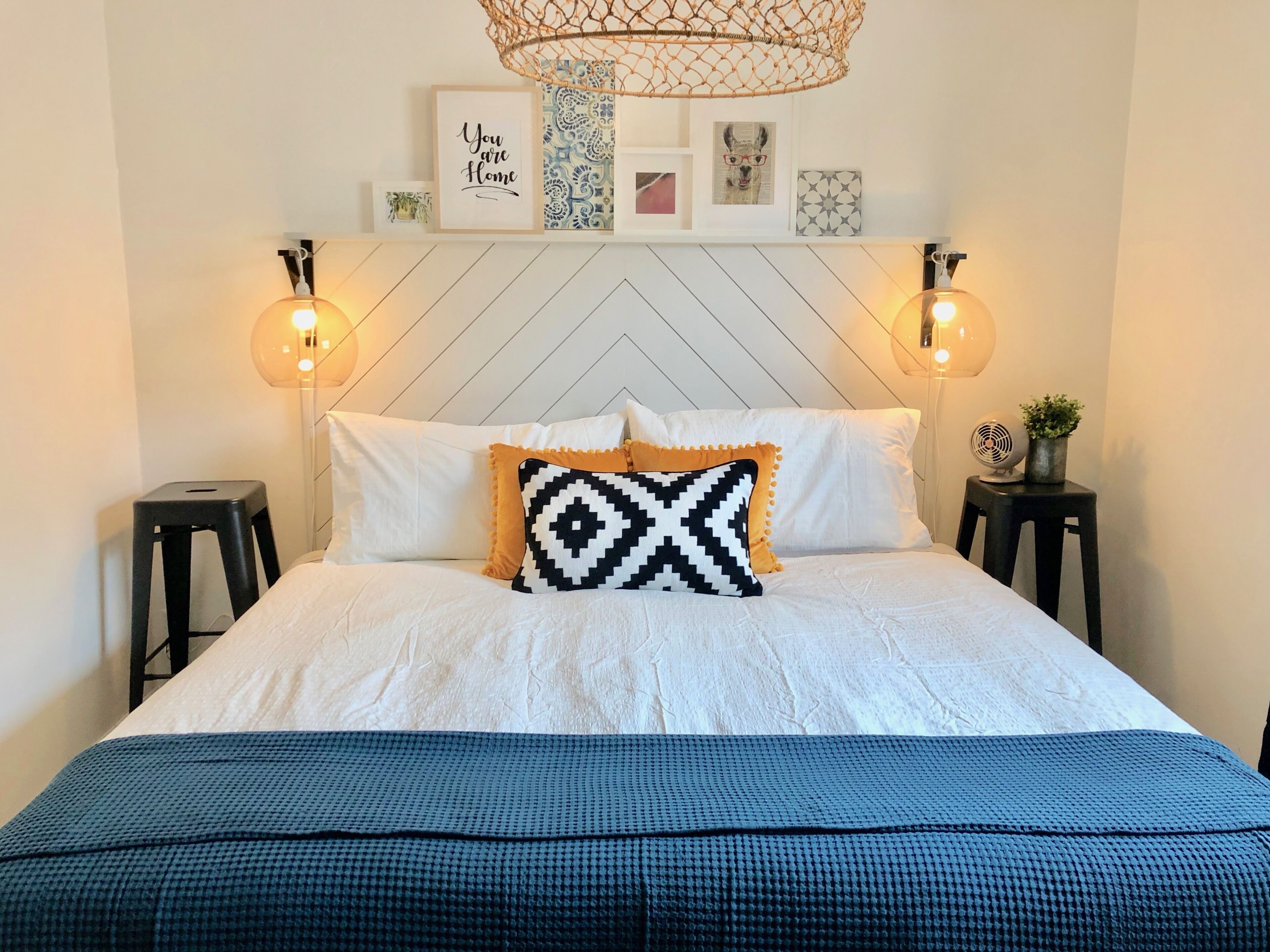 Ein ordentlich bezogenes Bett mit einem gemusterten Kopfkissen, zwei Nachttischlampen und einer Wand mit gerahmten Bildern.