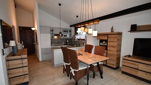 A modern kitchen with a dining area, wooden cabinets, and a TV. - Holiday home Kenter Tossens (Butjadingen)