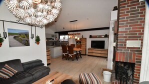 A modern living room with a black sofa, a wooden coffee table, and a striped ottoman. A dining area with a table and chairs is visible in the background. - Holiday home Kenter Tossens (Butjadingen)