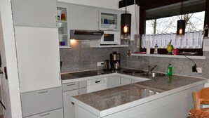 A modern kitchen with white cabinets, a granite countertop, a microwave, a coffee maker, and a window with a view of trees. - Holiday home Kenter Tossens (Butjadingen)