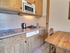 Une cuisine compacte avec des meubles en bois, un four à micro-ondes encastré, une bouilloire, un évier et une table à manger en bois.