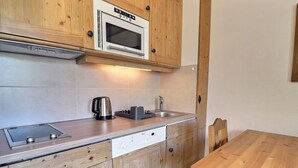 Eine kleine Küche mit Holzausstattung, einer eingebauten Mikrowelle, einem Wasserkocher, einer Spüle und einem Holztisch.