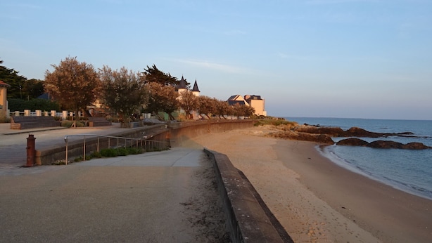 Un paseo marítimo con barandilla de piedra, una playa arenosa y vistas al mar.