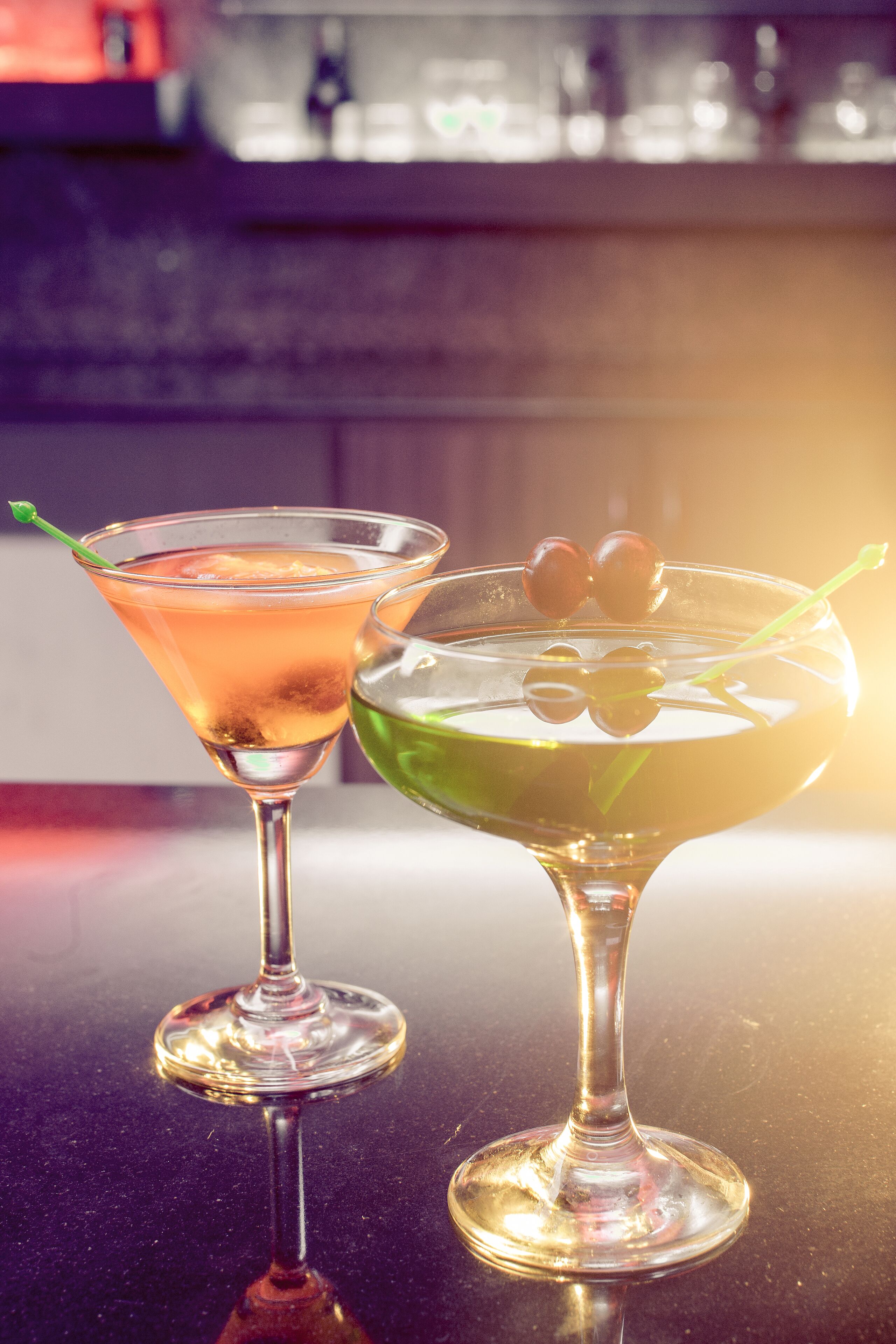 Due bicchieri di martini su una superficie riflettente, con sfondo sfocato.