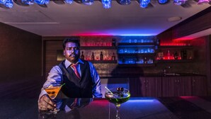 Eine Bar mit Bartender, einer Theke und Regalen mit Flaschen im Hintergrund.
