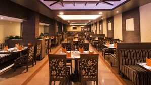 Ein geräumiges Restaurant mit mehreren Essbereichen, darunter Sitzecken und Tische, jeweils mit orangefarbenen Servietten und Speisekarten bestückt.