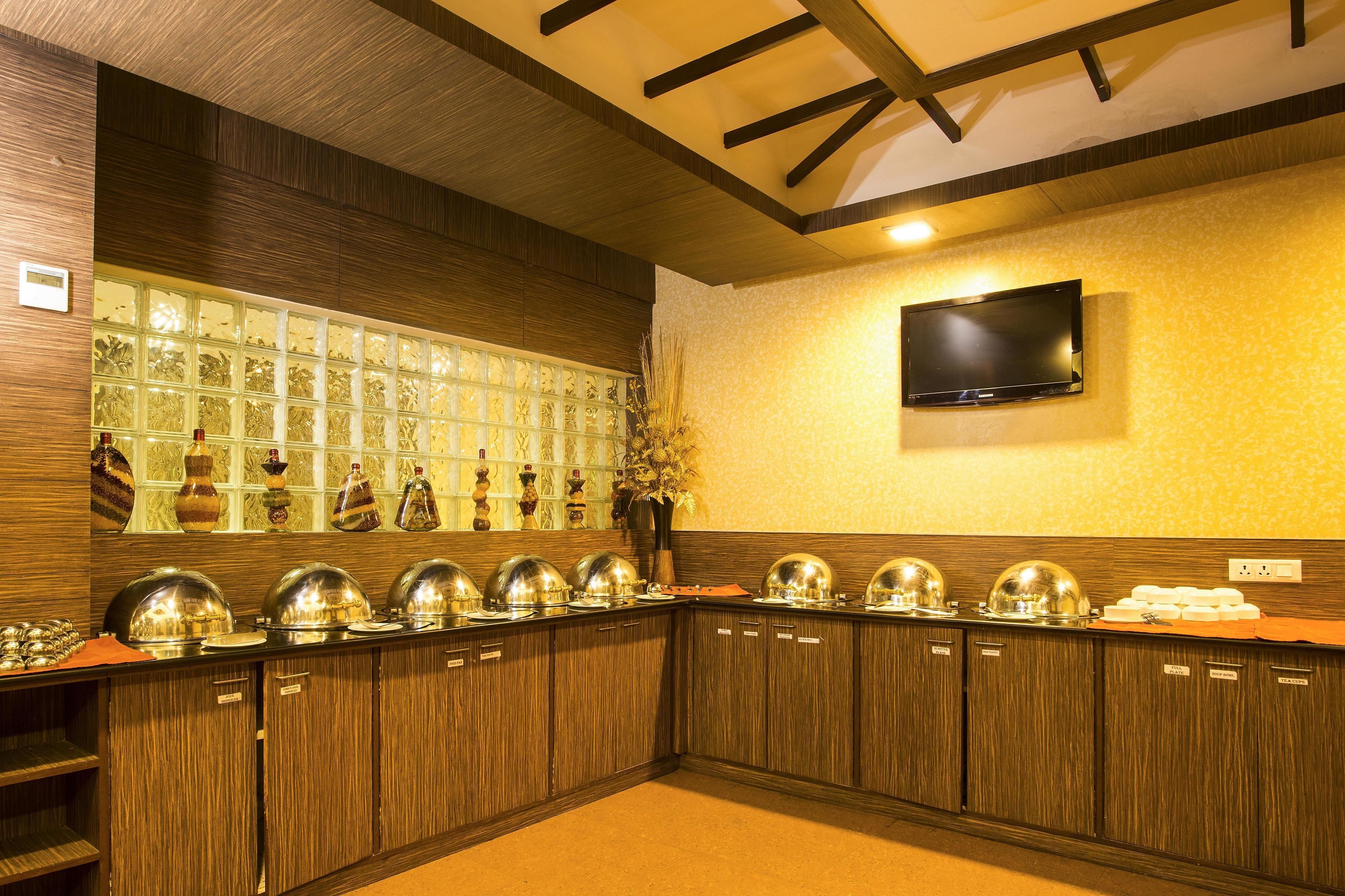 Buffet montado com várias estações de serviço, uma televisão na parede e uma parede decorativa com painéis de vidro.