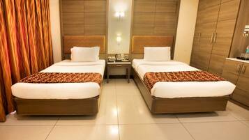 A hotel room with two beds, wooden headboards, a nightstand, and a wardrobe.