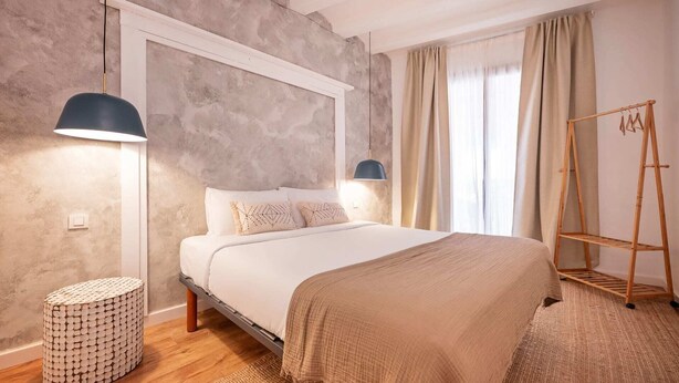 Una camera da letto con un letto, abat-jour, un comodino in legno, un appendiabiti e un tappeto decorato.