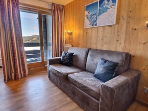 Ein gemütliches Zimmer mit einem braunen Ledersofa, gestreiften Vorhängen und einem großen Fenster mit Blick auf eine verschneite Landschaft.