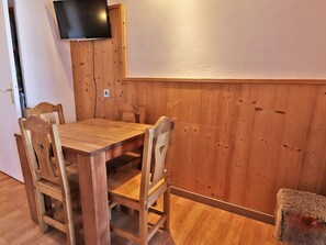 Ein Holztisch mit vier Stühlen, ein an der Wand befestigter Fernseher und ein kleiner Hocker.