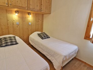 Two single beds with white bedding and plaid pillows in a room with wooden panel walls and built-in lighting.