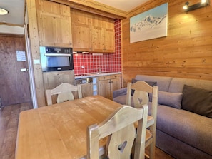 A wooden interior with a dining table, chairs, a sofa, and a kitchen area with a microwave and red tiles. - Charming Méribel Studio - Central, Pets Allowed (Méribel)