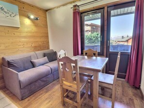 Ein Zimmer mit einer Holzwand, einem grauen Sofa, einem Holzesstisch mit Stühlen und einem Fenster mit Vorhängen.