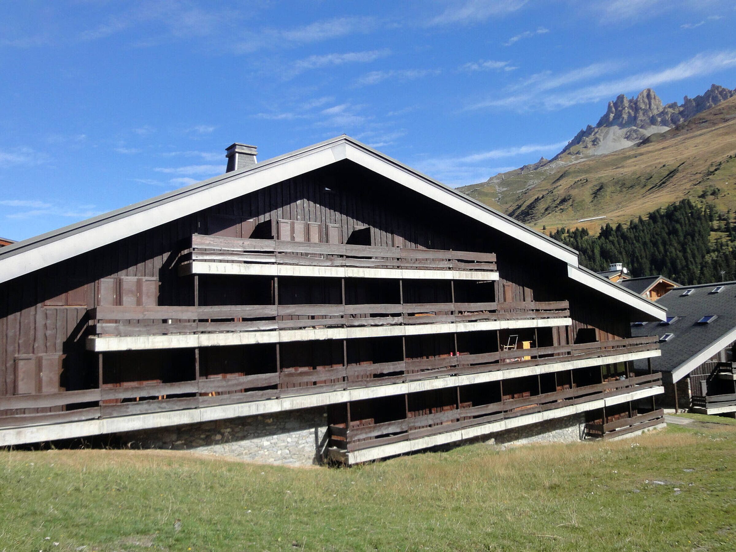 A wooden chalet with a sloped roof and multiple balconies, set against a mountainous backdrop.