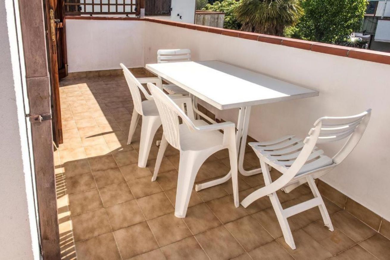 A patio with a white table and chairs, a tiled floor, and a view of greenery.