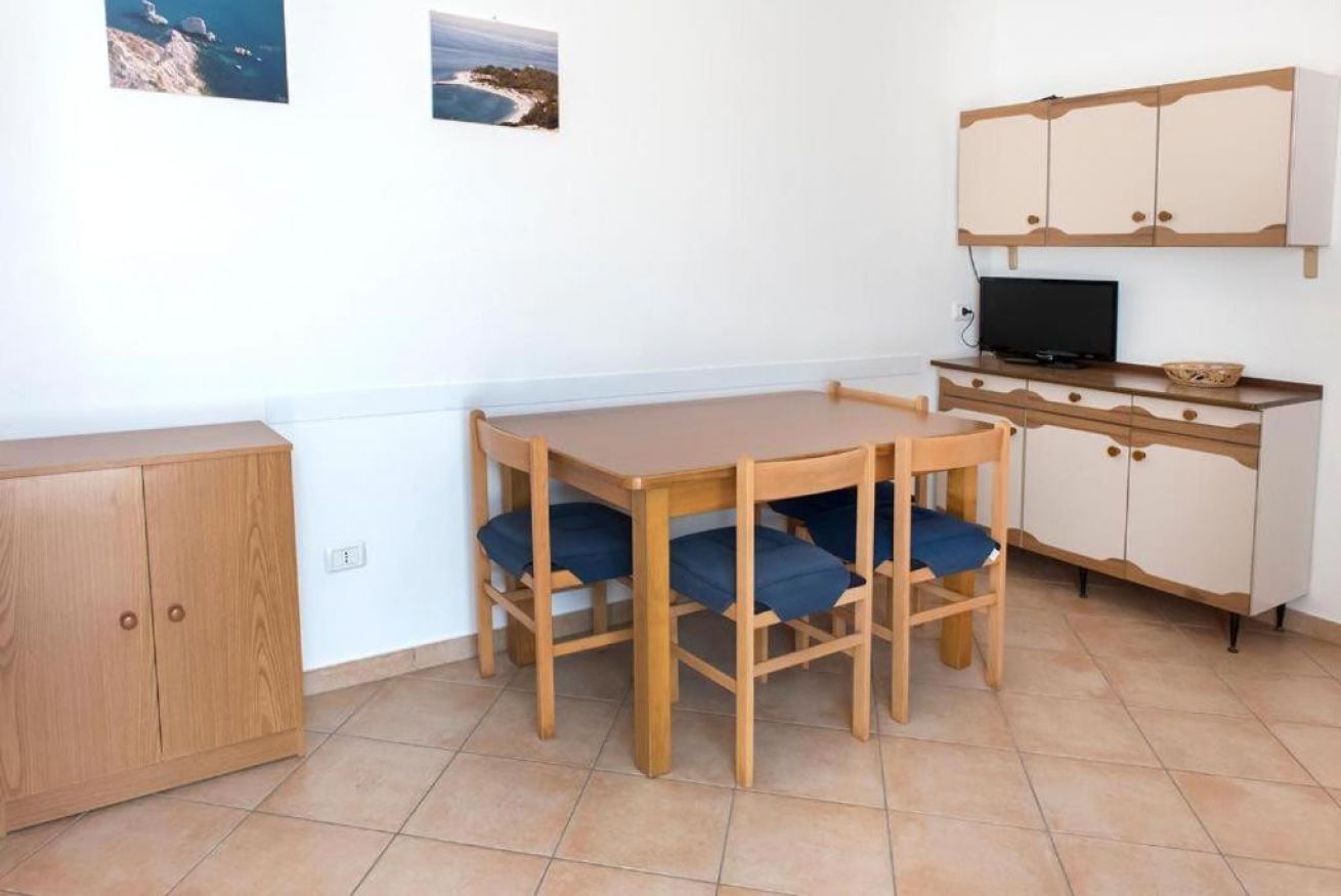 A small, tidy room with a wooden table and chairs, a television, and a cabinet.