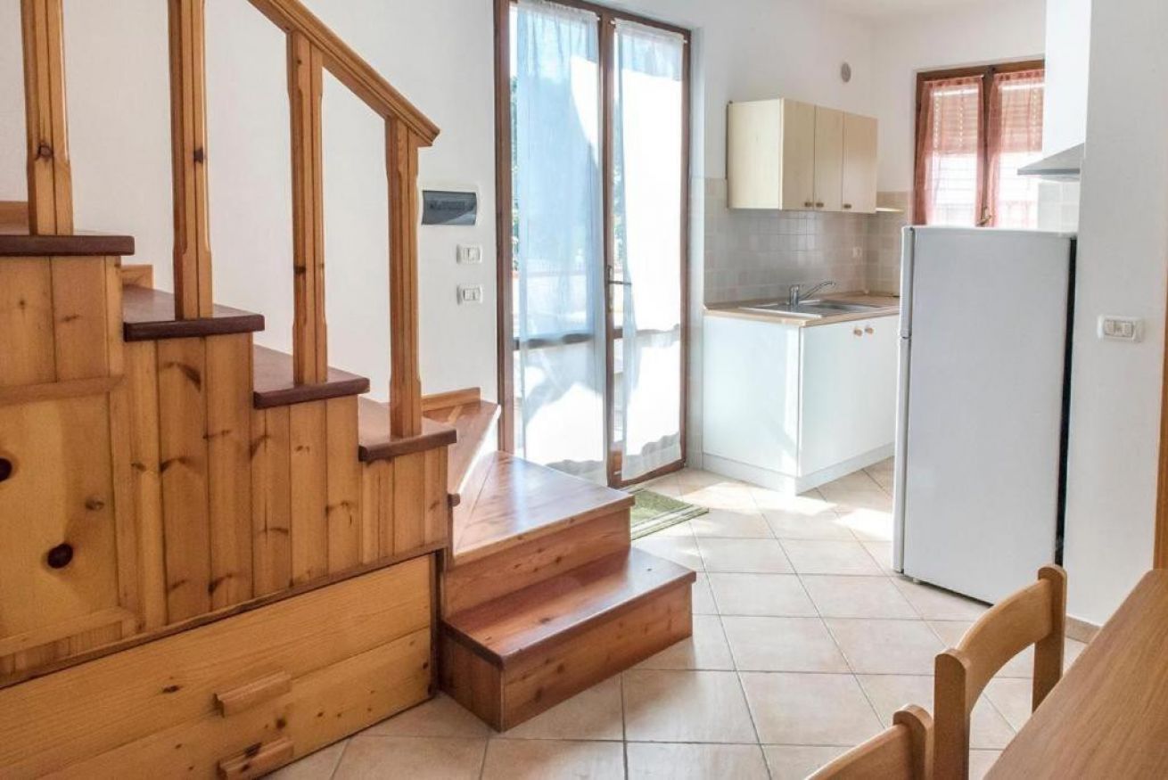 Een keuken met een koelkast, een spoelbak en houten trap naar een balkon.