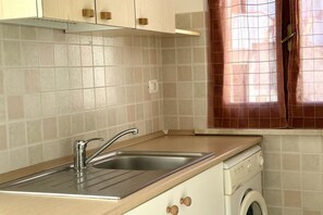 A kitchen with a stainless steel sink, wooden cabinets, a washing machine, and a tiled backsplash. - M035 - Marcelli, three-room apartment with terrace and a / c (Marcelli)