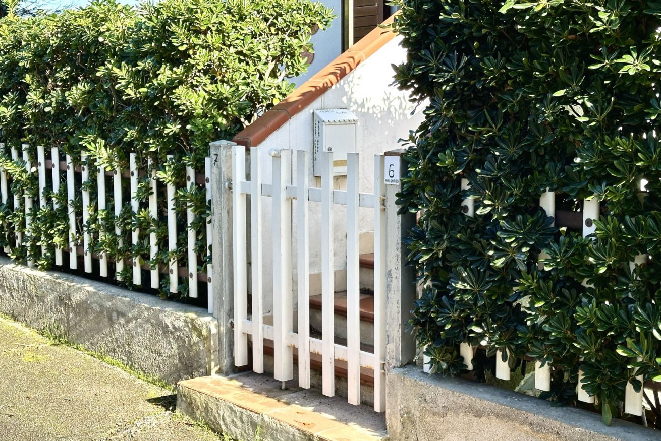 A white gate with a wooden handrail, a white picket fence, and green foliage.