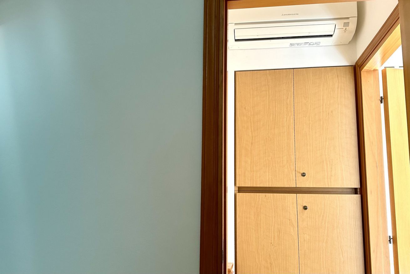 A room with a wooden wardrobe, a white wall, and an air conditioning unit.
