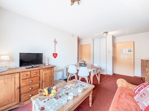 A cozy living room with a television, wooden furniture, a dining table with chairs, and a red heart decoration on the wall. - Bâtiment B by Interhome (Le Corbier)