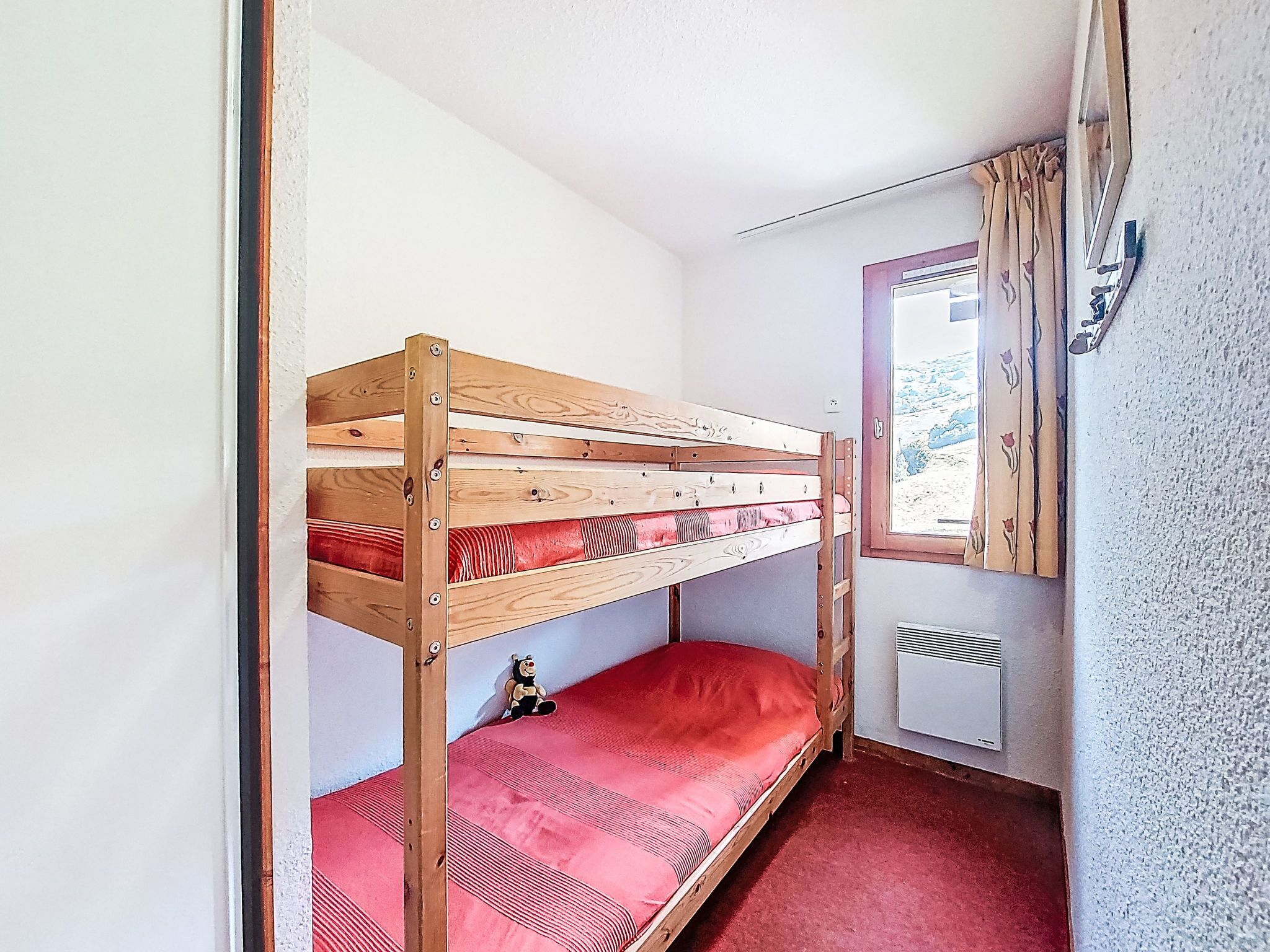 A bunk bed with a red mattress in a small room with a window and a radiator.