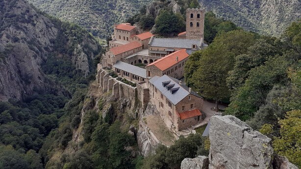 Ein historisches Steinhaus mit mehreren Stockwerken und einem Turm, gelegen auf einem Berg inmitten dichtem Wald.