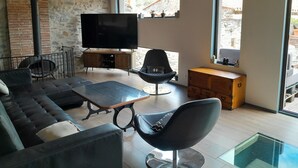 Ein modernes Wohnzimmer mit Steinwand, Flachbildfernseher, Sofa, Couchtisch und einem Esstisch mit Glasplatte.