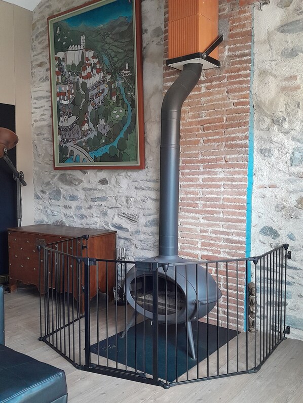 Une pièce avec un mur en pierre, une armoire en bois, une rambarde en métal et un grand tableau représentant un village.