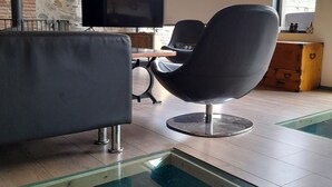 Ein modernes Wohnzimmer mit Steinwand, Flachbildfernseher, Ledersessel in Schwarz, Glastisch und Holzschrank.