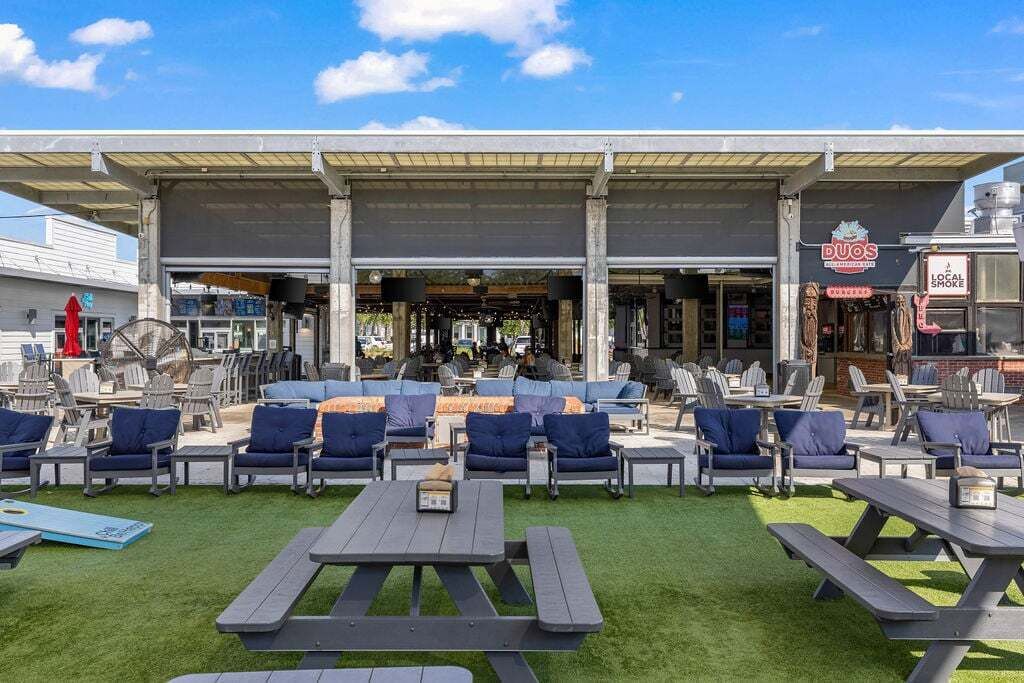 Een terras met tafels en stoelen, een overdekte patio en een zichtbare bar.