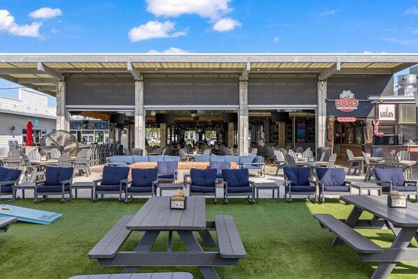 Un espacio al aire libre con mesas y sillas, un porche cubierto y una zona de bar visible.
