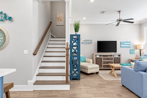 A modern living room with a staircase, a flat-screen TV, a blue sofa, and a wooden coffee table.