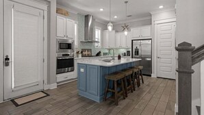 Una cocina moderna con armarios blancos, una isla azul, electrodomésticos de acero inoxidable y taburetes de madera.