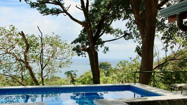 Una piscina con vista sull'oceano, circondata da alberi e un solarium in pietra.
