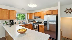 A modern kitchen with wooden cabinets, stainless steel appliances, and a bowl of lemons on the counter. - Coastal Place - BEST location in Downtown (Anchorage)