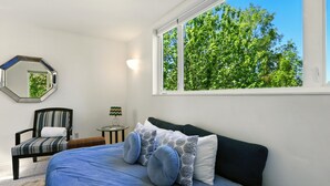 A bedroom with a bed, a chair, a round table, a lamp, and a window with a view of trees. - Coastal Place - BEST location in Downtown (Anchorage)