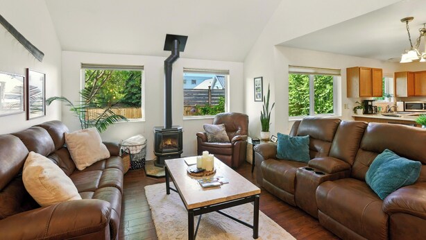 A spacious living room with a fireplace, leather sofas, a coffee table, and large windows offering a view of the outdoors. - Coastal Place - BEST location in Downtown (Anchorage)