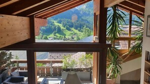 A room with a large window offering a view of a green landscape and a wooden ceiling structure. - Chalet Abendrot apARTments by Interhome (Grindelwald)