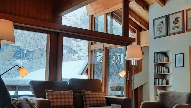 A cozy living room with a sofa, armchairs, a coffee table, and a bookshelf. Large windows offer a view of snowy mountains. - Chalet Abendrot apARTments by Interhome (Grindelwald)