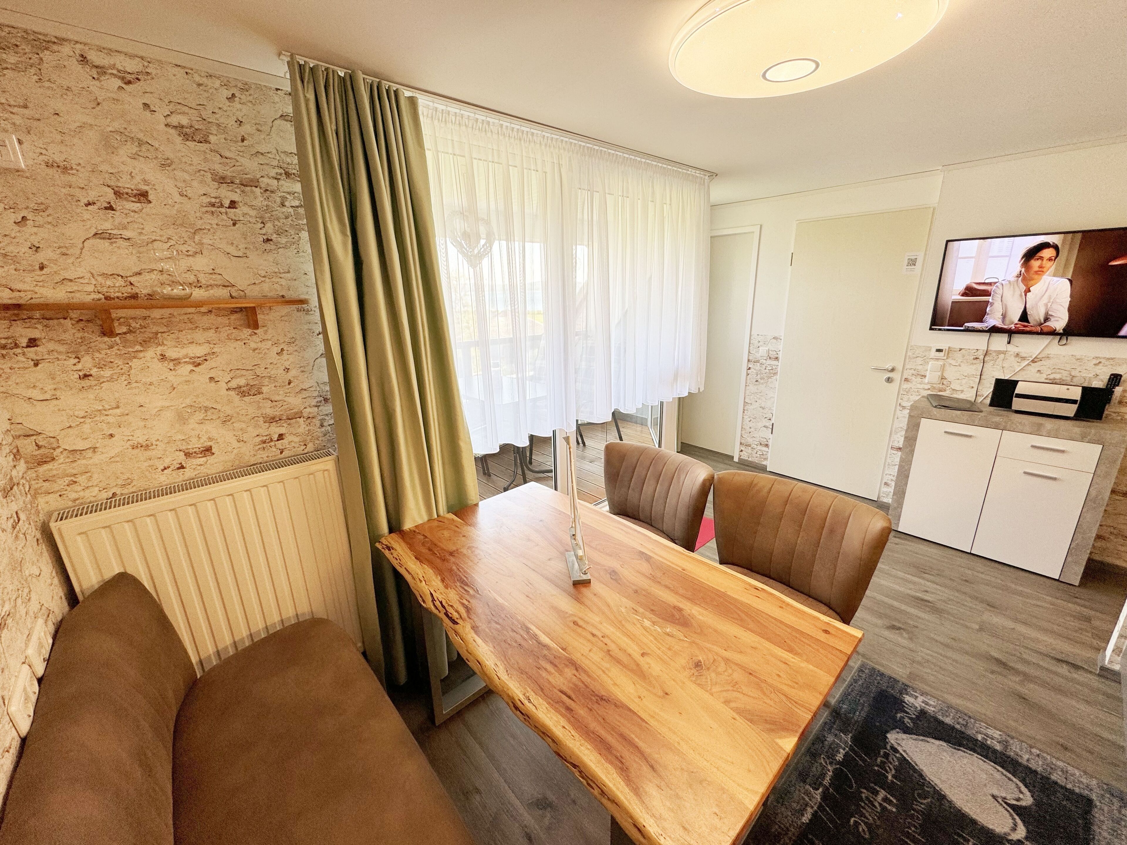 Una sala de estar acogedora con una mesa de comedor de madera, dos sofás marrones, un televisor en la pared y una cocina con un armario blanco y una encimera.