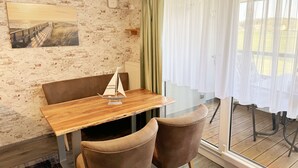 A dining area with a wooden table and two chairs, a painting on the wall, and a view through a window with sheer curtains. - Apartment 06 with balcony and view of the Bodden - MR: Haus Inselperle with view of the (Mönchgut)