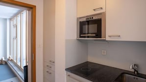 A compact kitchen with a built-in microwave, a stainless steel sink, and a black countertop. - Chesa Corvatsch 111 - Champfer by Interhome (Champfer)