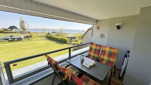 Un balcón con mesa y sillas, vista a un campo cubierto de césped y una casa, junto a un pequeño jardín.
