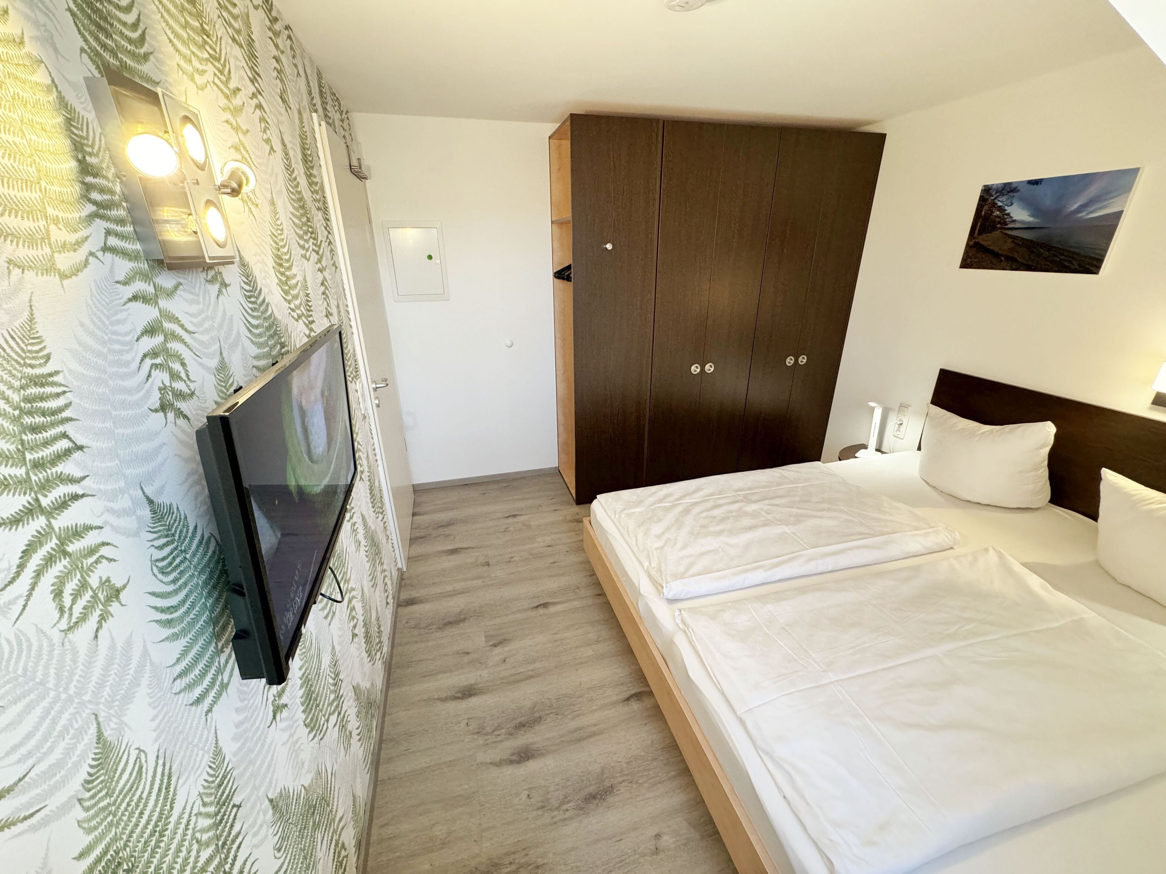 Un dormitorio con cama, armario, televisor montado en la pared y un cuadro.