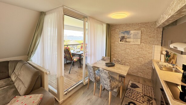 Una sala acogedora con un sofá, una mesa de comedor con sillas, una zona de cocina con un fregadero y vistas al exterior a través de un ventanal corredero.